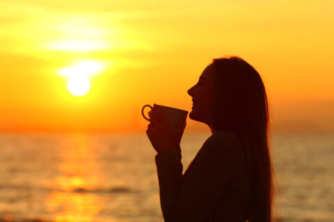 Woman silhouette holding mug at sunset on the beach
