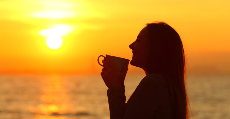 Woman silhouette holding mug at sunset on the beach
